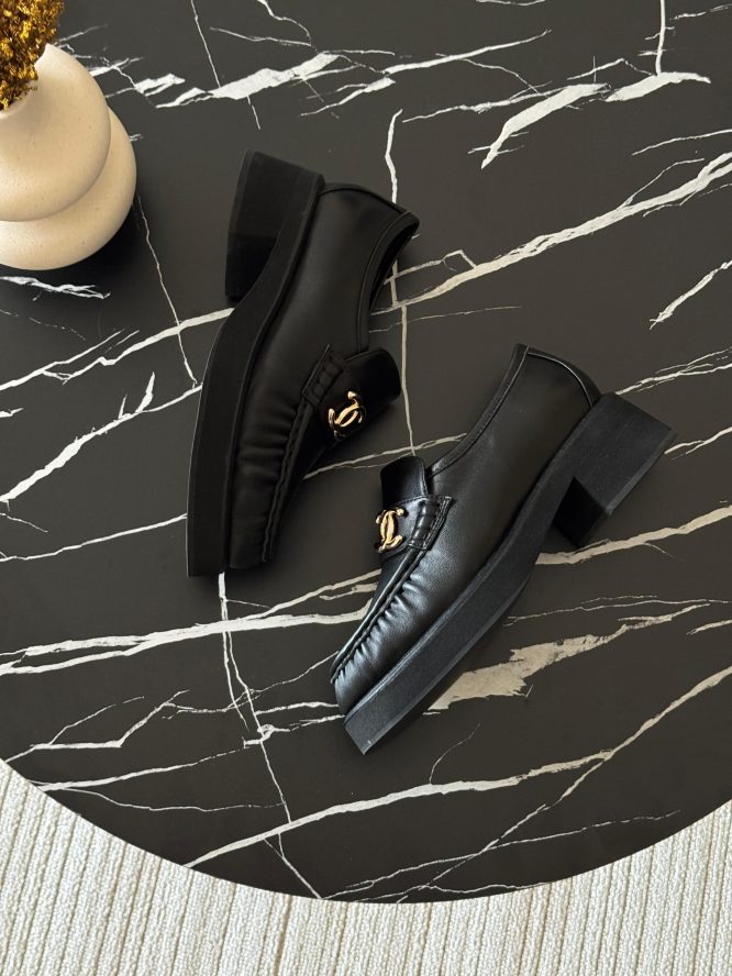 Black leather Chanel loafers with gold-tone logo detailing, offering a sleek and elegant design.