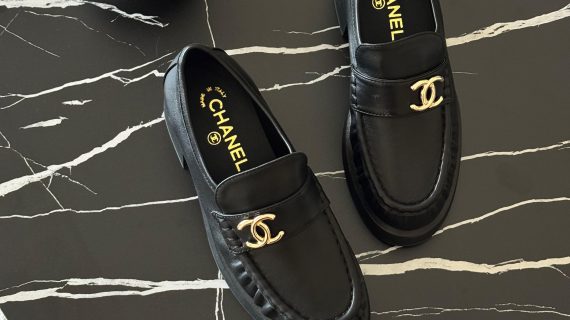Black leather Chanel loafers with gold-tone logo detailing, offering a sleek and elegant design.