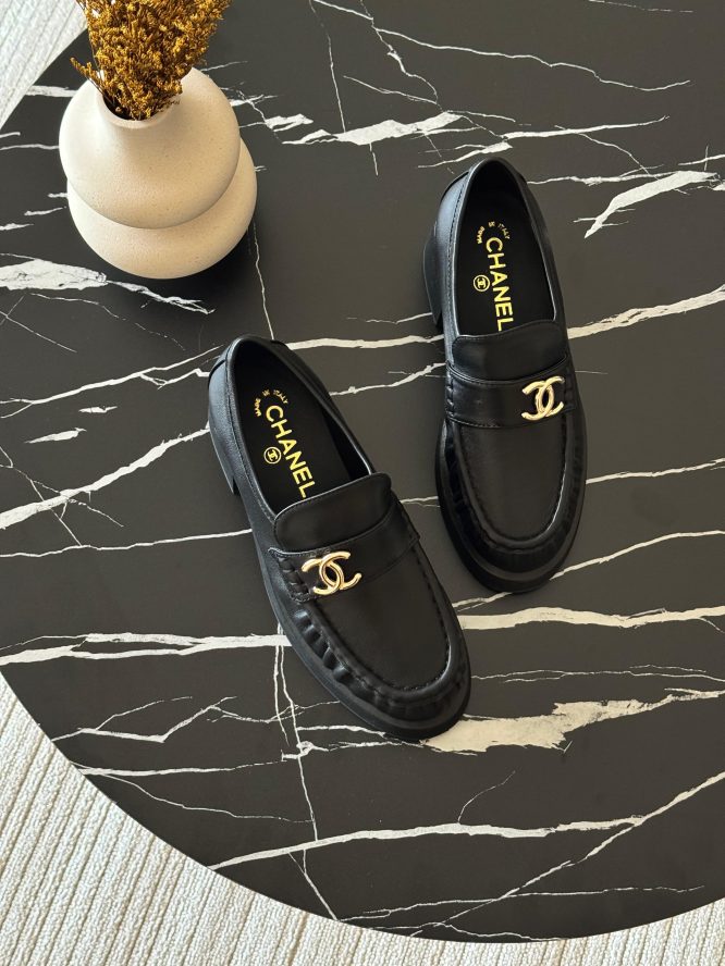 Black leather Chanel loafers with gold-tone logo detailing, offering a sleek and elegant design.