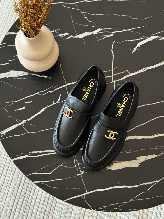 Black leather Chanel loafers with gold-tone logo detailing, offering a sleek and elegant design.